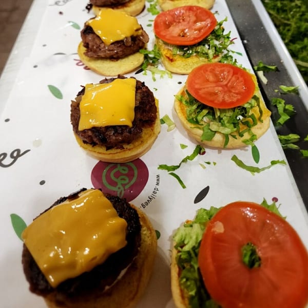 A white tray holds several vegan sliders, some with cheese, others with lettuce and tomato.