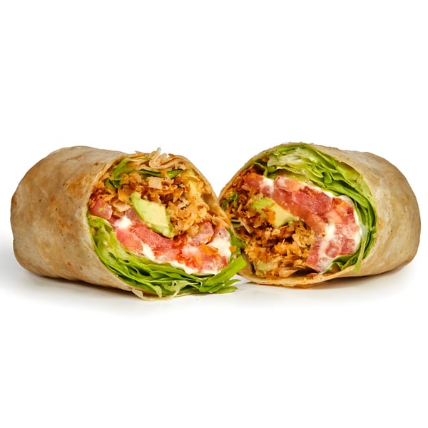 Vegan wrap, cut in half, filled with plant-based protein, lettuce, tomato, avocado, and sauce.