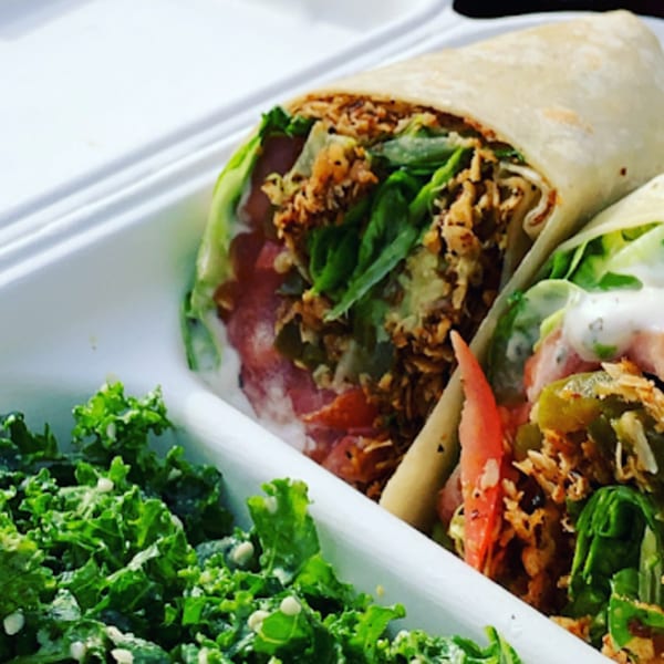 Two vegan wraps filled with lettuce, tomatoes, and plant-based protein, served with a side of kale salad.