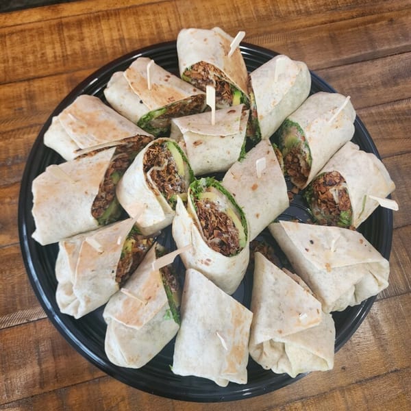 A black platter filled with many vegan wraps, cut in half, revealing avocado and plant-based protein.