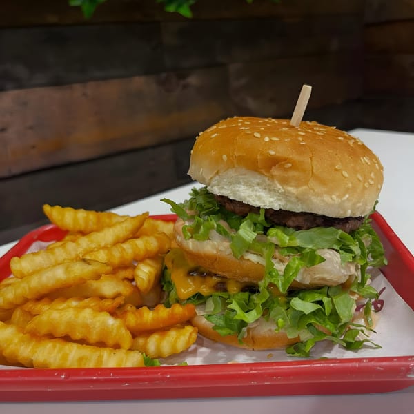 Vegan double cheeseburger with lettuce and sauce, served with crinkle-cut fries on a red tray.