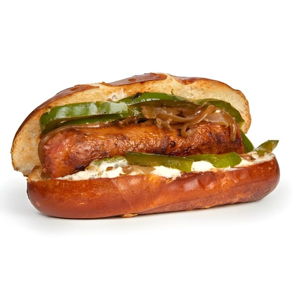Daily Veg's vegan sausage sandwich with green peppers, caramelized onions, and white sauce on a pretzel bun.
