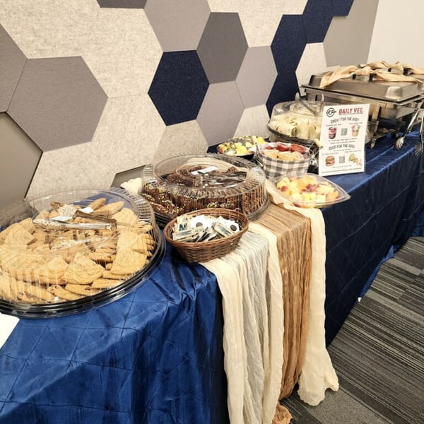 A Daily Veg catering spread with cookies, brownies, fruit, and wraps on a blue tablecloth.